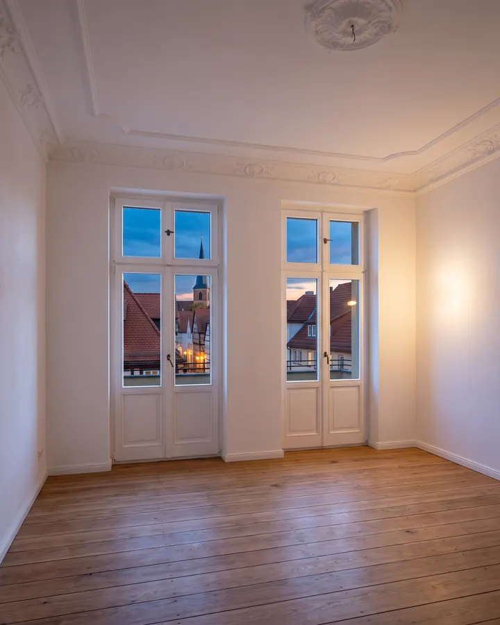 Leere Altbauwohnung mit Stuckdecke, Dielenboden und Blick auf Ziegeldächer